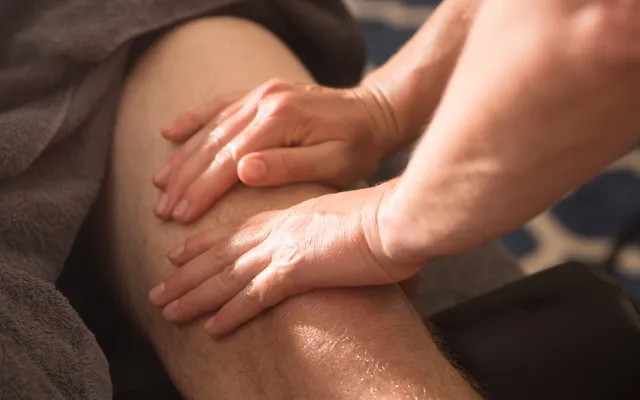 A sports massage therapist working along a client's hamstring with both hands
